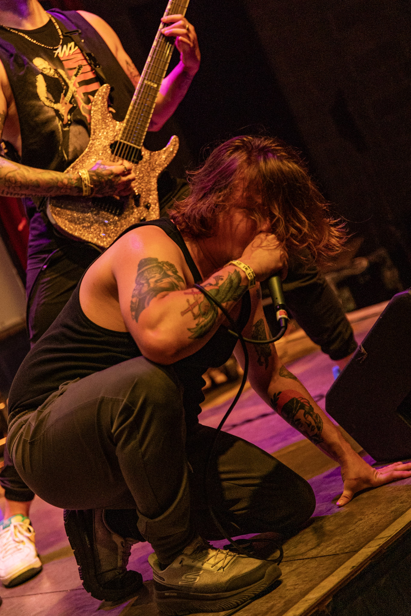 Vocalist crouching alongside guitarist under warm stage lighting